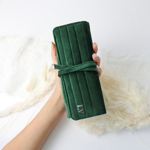 May include: A dark green velvet jewelry roll with a quilted design and a silver clasp. The roll has a personalized monogram "LV" in silver lettering.