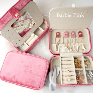 May include: Pink velvet jewelry box with a mirror and multiple compartments for storing rings, earrings, necklaces, and bracelets. The box has the words "Barbie Pink" printed on the top.