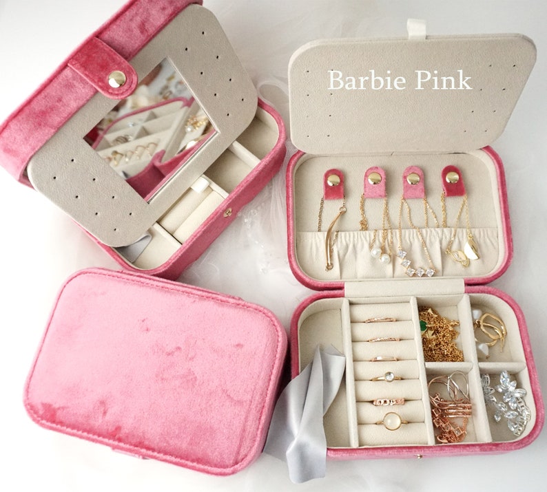 May include: Pink velvet jewelry box with a mirror and multiple compartments for storing rings, earrings, necklaces, and bracelets. The box has the words "Barbie Pink" printed on the top.