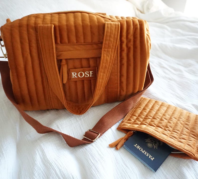 May include: A brown quilted travel bag with a shoulder strap and a matching smaller pouch. The bag has the name "ROSE" embroidered on the front. The pouch contains a passport.