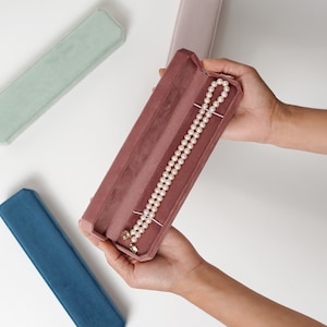 May include: A pink velvet jewelry box with a pearl necklace inside. The box is open and the necklace is visible.