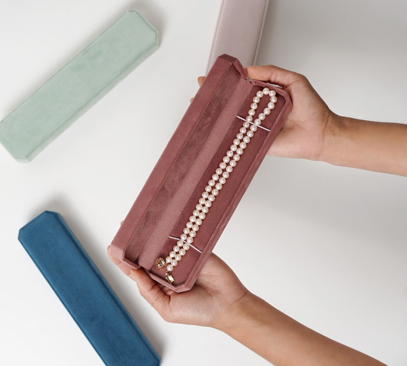 May include: A pink velvet jewelry box with a pearl necklace inside. The box is open and the necklace is visible.