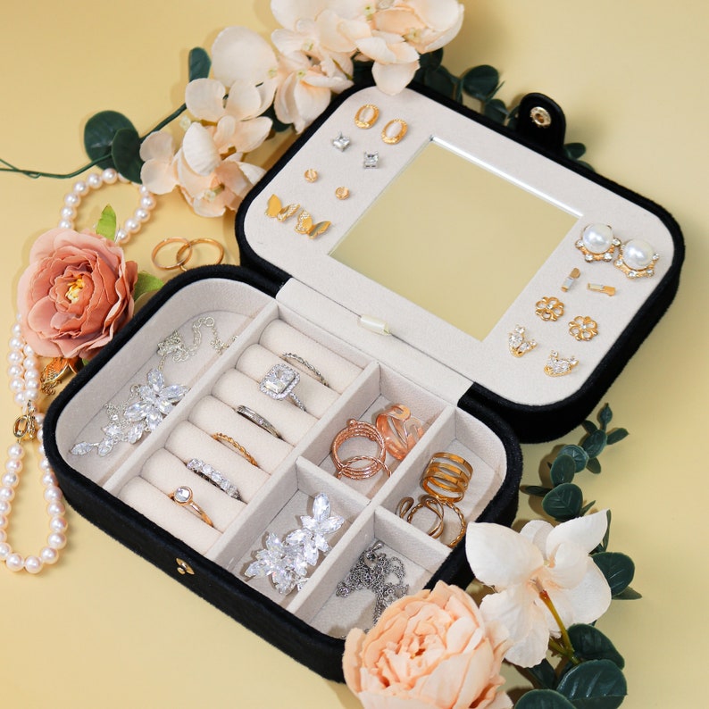 May include: Black velvet jewelry box with a mirror and multiple compartments for storing rings, earrings, and necklaces. The box is open and filled with various gold and silver jewelry.