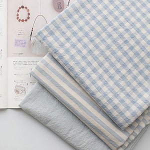 May include: Three pieces of fabric in different patterns: a blue and white gingham, a blue and white striped, and a solid light blue. The fabric is folded and stacked.