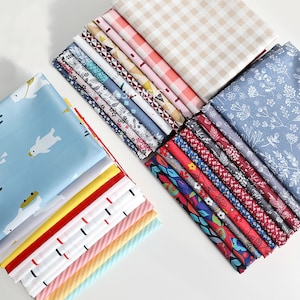 May include: A collection of fabric swatches in various patterns and colors, including floral, geometric, and plaid designs. The fabrics are arranged in two stacks, with one stack featuring a light blue fabric with a white polar bear print.