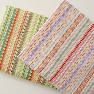 May include: Two pieces of striped fabric in green, orange, red, and white. The fabric is folded in half and the two pieces are layered on top of each other.