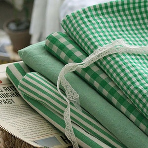 Könnte beinhalten: Ein Stapel grüner und weißer karierter Stoff mit einem weißen Spitzenband. Der Stoff ist gefaltet und in einem Weidenkorb mit einer Zeitung darauf gelegt. Die Schlagzeile der Zeitung lautet "03 News Heading Rits Adip Singra Tempas".