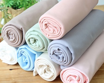 May include: Eight rolls of fabric in various colors, including beige, light green, light blue, white, gray, and pink. The fabric is rolled up and stacked on a wooden surface.