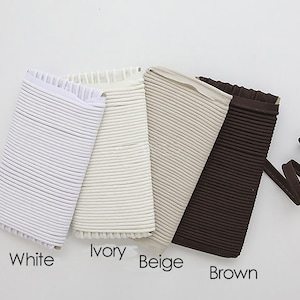 May include: Four samples of elastic cord in different colors: white, ivory, beige, and brown. The cord is ribbed and has a frayed edge.