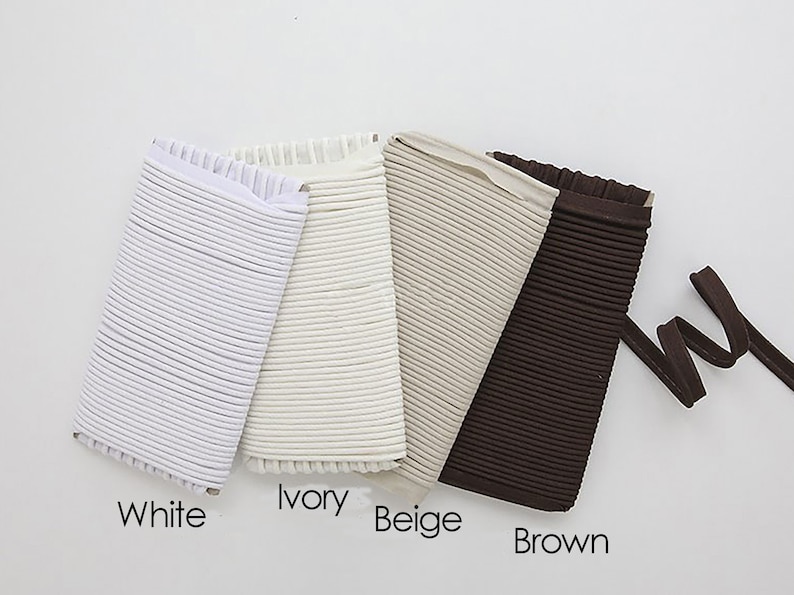 May include: Four samples of elastic cord in different colors: white, ivory, beige, and brown. The cord is ribbed and has a frayed edge.