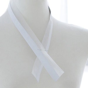 Puede incluir: Cinta de satén blanca atada en un nudo simple, creando un lazo decorativo. La cinta se muestra en un maniquí blanco.