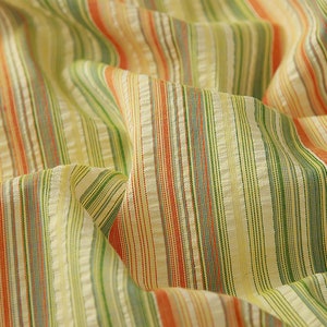 May include: Close-up of a striped fabric with orange, green, and white stripes. The fabric is woven and has a textured surface.