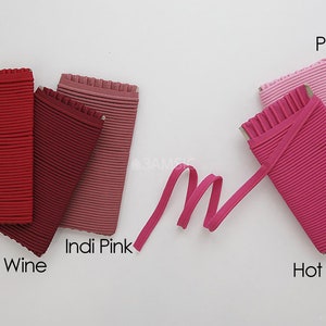 May include: Five different colors of ribbed elastic fabric, including red, wine, Indi Pink, pink, and hot pink. The fabric is folded and arranged in a row on a white surface.