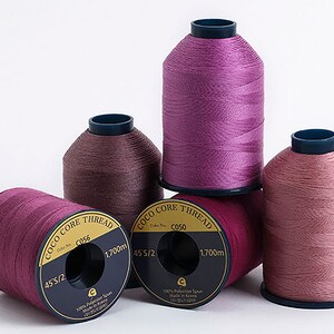 Puede incluir: Cuatro carretes de hilo rosa, malva y burdeos etiquetados "Coco Core Thread" con el texto "45'S/2", "CC050", "1.700 m" y "100% Polyester Spun Made in Korea".