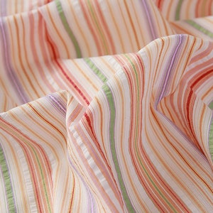 May include: Close-up of a white fabric with multi-colored stripes in shades of pink, red, green, and purple.