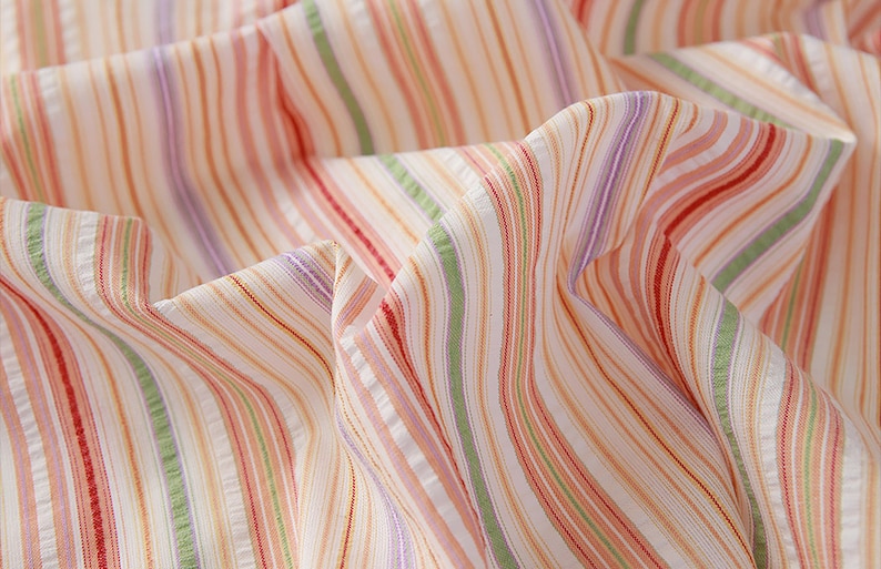 May include: Close-up of a white fabric with multi-colored stripes in shades of pink, red, green, and purple.