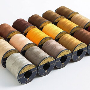 Puede incluir: Una colecci&oacute;n de 15 carretes de hilo Coco Core en varios tonos de marr&oacute;n, beige y amarillo. Cada carrete est&aacute; etiquetado con "Coco Core Thread" y tiene una etiqueta negra y dorada con el texto "Coco Core Thread" y "1000m".