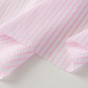 May include: Pink and white striped fabric with a textured weave. The fabric is folded over itself, showing the pattern on both sides.