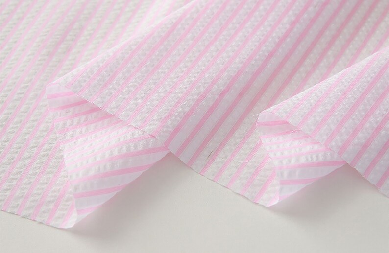 May include: Pink and white striped fabric with a textured weave. The fabric is folded over itself, showing the pattern on both sides.