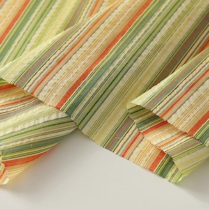 May include: Close-up of a striped fabric with orange, green, and yellow stripes. The fabric is folded in half, showing the pattern on both sides.