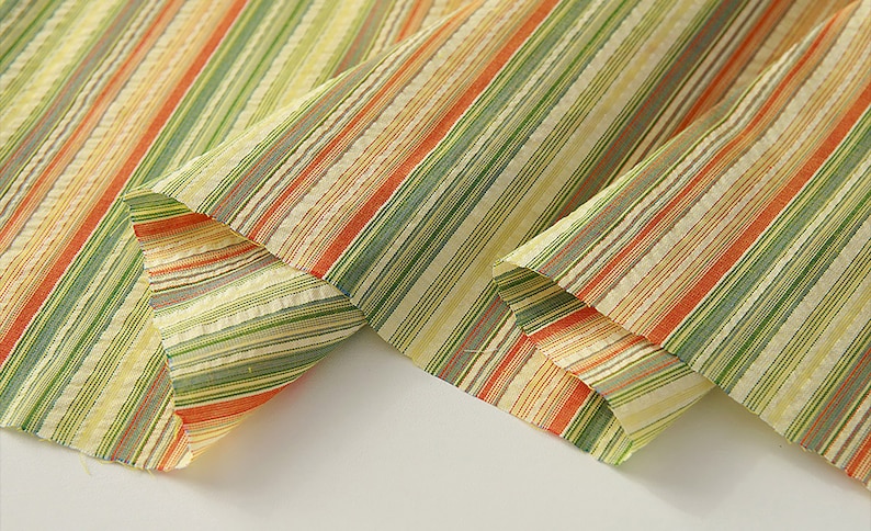 May include: Close-up of a striped fabric with orange, green, and yellow stripes. The fabric is folded in half, showing the pattern on both sides.