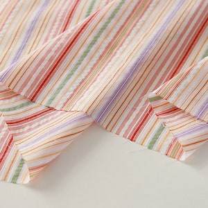 May include: Close-up of a multi-colored striped fabric with a white background. The fabric is folded in half, showing the stripes on both sides.
