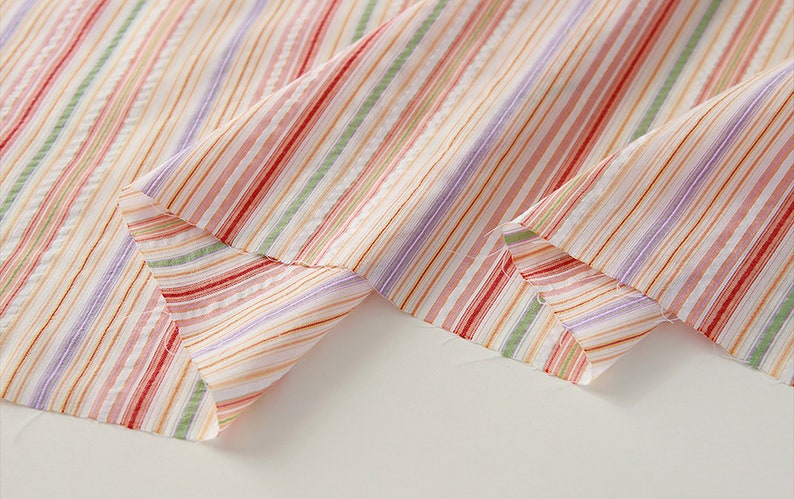 May include: Close-up of a multi-colored striped fabric with a white background. The fabric is folded in half, showing the stripes on both sides.
