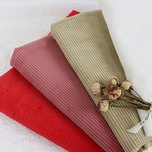 Op de afbeelding: Vier verschillende kleuren corduroy stofstalen. De kleuren zijn rood, roze, beige en wit. De stof is geribbeld en heeft een zachte textuur.