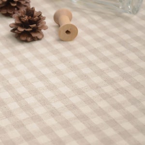 May include: A close-up of a white and brown gingham tablecloth with a wooden spool and pine cones on top.