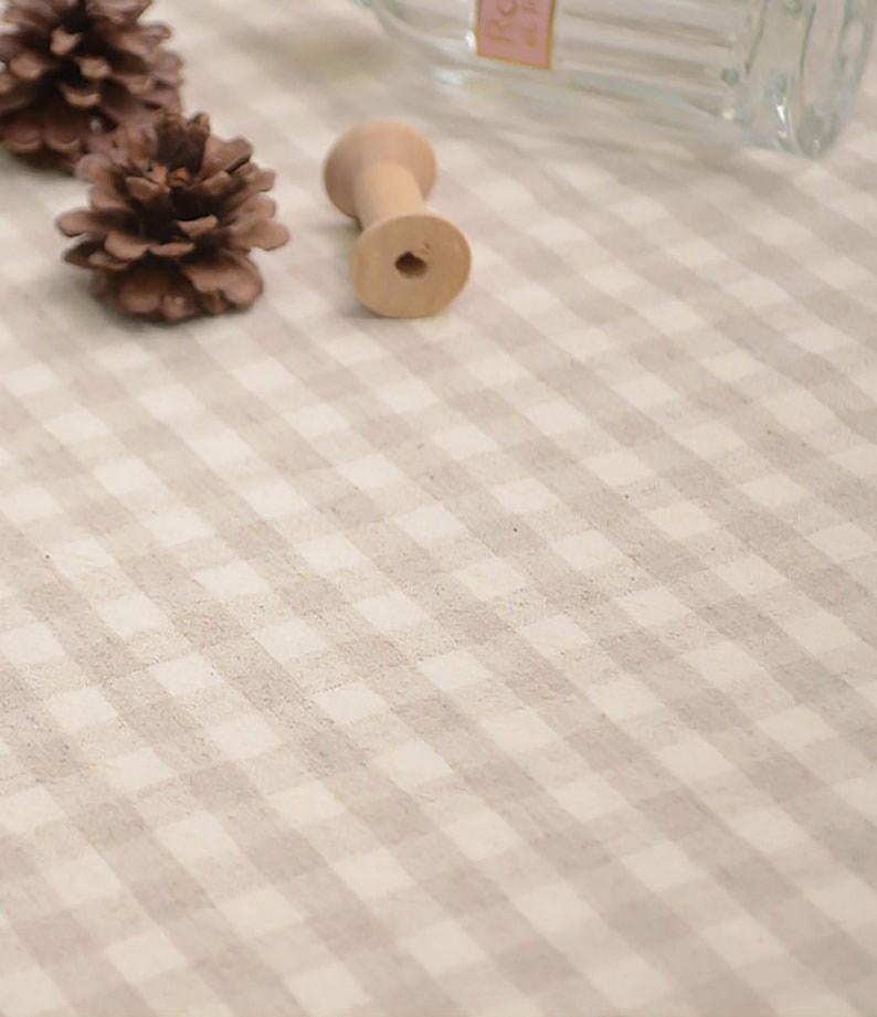 May include: A close-up of a white and brown gingham tablecloth with a wooden spool and pine cones on top.