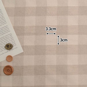 May include: Beige and white gingham fabric with a 3.3 inch by 3 inch square marked out. The fabric has a subtle texture.