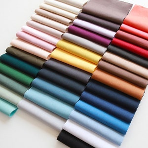 Puede incluir: Una colección de muestras de tela en varios colores, incluyendo beige, rosa, amarillo, verde, azul y rojo. Las muestras están dispuestas en un patrón escalonado, con la muestra superior siendo beige y la muestra inferior siendo roja.