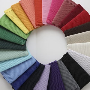 May include: A collection of 20 fabric swatches arranged in a circle, showcasing a variety of colors and textures. The swatches are all pleated and have a subtle sheen.