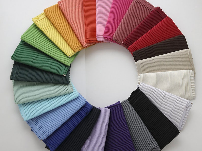 May include: A collection of 20 fabric swatches arranged in a circle, showcasing a variety of colors and textures. The swatches are all pleated and have a subtle sheen.