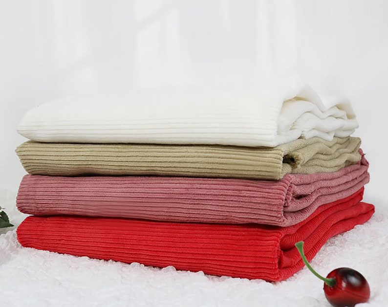 Op de afbeelding: Vier verschillende kleuren corduroy stof gestapeld op elkaar. De kleuren zijn wit, beige, roze en rood.