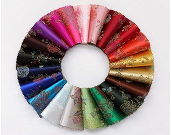 Pode incluir: Uma variedade de amostras de tecido em diferentes cores e padrões. As amostras estão dispostas em um círculo, com as cores que vão do rosa ao vermelho, ao laranja, ao amarelo, ao verde, ao azul e ao roxo. Cada amostra apresenta um design floral com detalhes dourados.