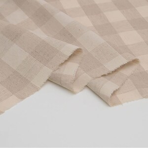 May include: Beige and white gingham fabric with a woven texture. The fabric is folded in a way that shows the pattern and texture.