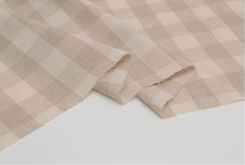 May include: Beige and white gingham fabric with a woven texture. The fabric is folded in a way that shows the pattern and texture.