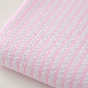 May include: Pink and white striped fabric with a textured weave. The fabric is folded and the stripes are running horizontally.