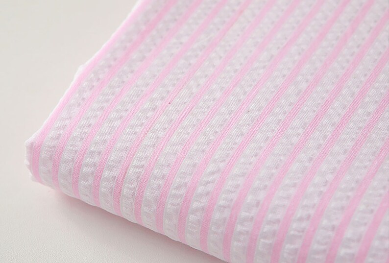 May include: Pink and white striped fabric with a textured weave. The fabric is folded and the stripes are running horizontally.