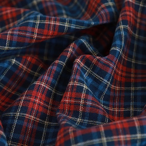 May include: Close-up of a blue and red plaid fabric with a subtle white thread woven throughout. The fabric is folded and creased, creating a textured look.