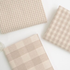 May include: Three pieces of beige and white gingham fabric with different sized checks.