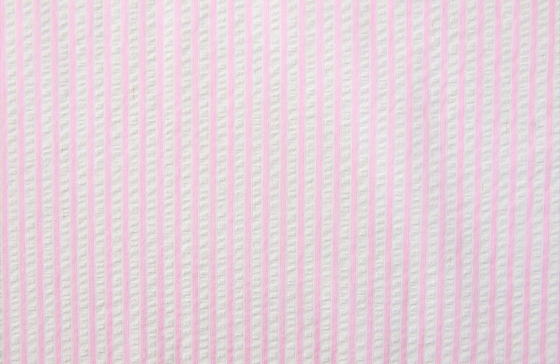 May include: White fabric with thin pink stripes. The fabric has a textured surface.