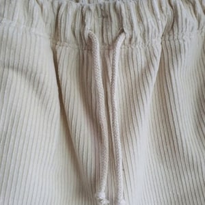 Op de afbeelding: Close-up van een paar off-white corduroy broeken met een trekkoord.