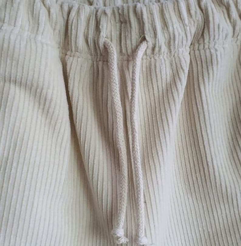 Op de afbeelding: Close-up van een paar off-white corduroy broeken met een trekkoord.