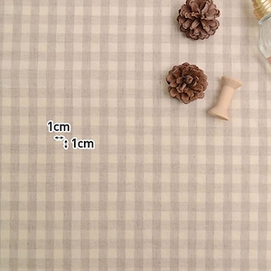 May include: A close-up of a beige and white gingham fabric with a 1 cm by 1 cm grid pattern. The fabric is textured and has a subtle sheen.
