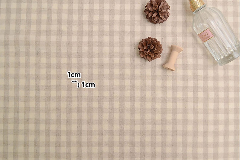 May include: A close-up of a beige and white gingham fabric with a 1 cm by 1 cm grid pattern. The fabric is textured and has a subtle sheen.