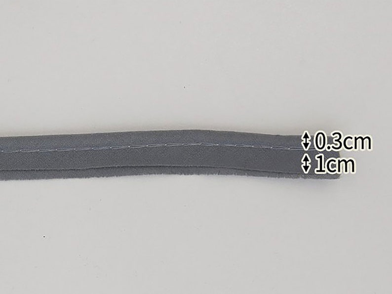 May include: Gray fabric trim with a stitched edge. The trim is 0.3 cm wide and 1 cm long.