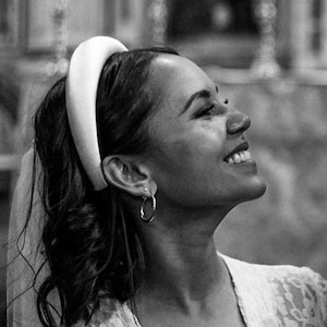 Può includere: Una donna con un abito di pizzo bianco e una fascia bianca. Sta sorridendo e guardando verso l'alto.