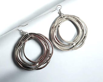 May include: A pair of silver hoop earrings with a unique, multi-layered design. The earrings are made of thin, twisted metal that creates a circular shape.